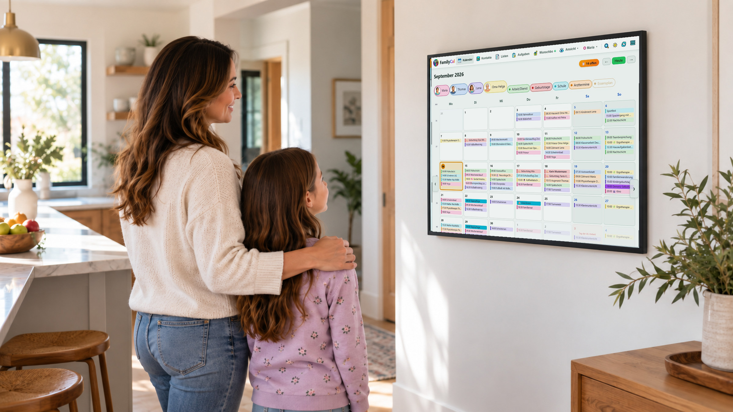 Mutter und Tochter stehen in der Küche vor einem Wandtablet, das den FamilyCal-Monatskalender zeigt: jede Person in ihrer eigenen Farbe